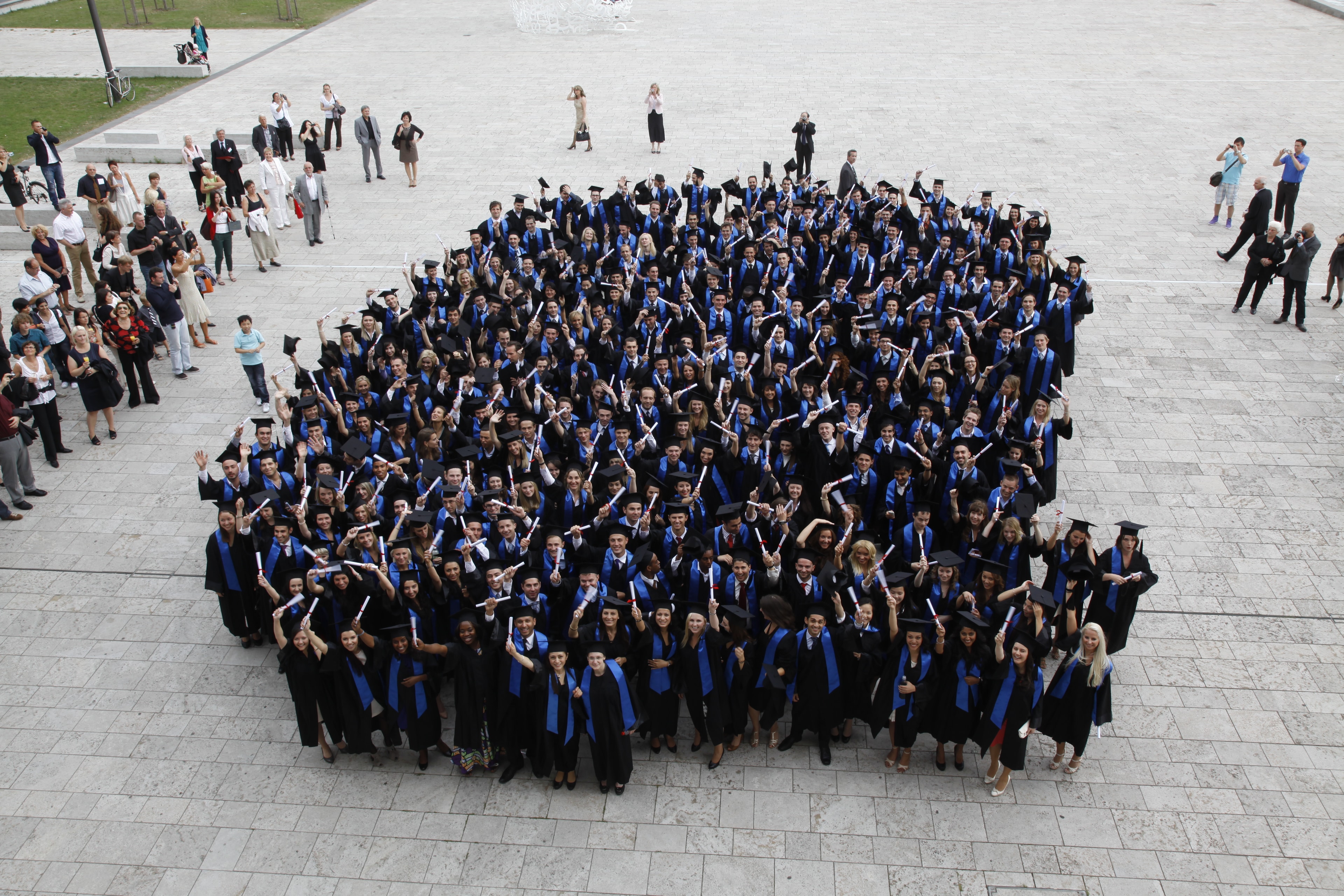 Absolventen mit Talaren und goldenen Schärpen vor historischem Schloss