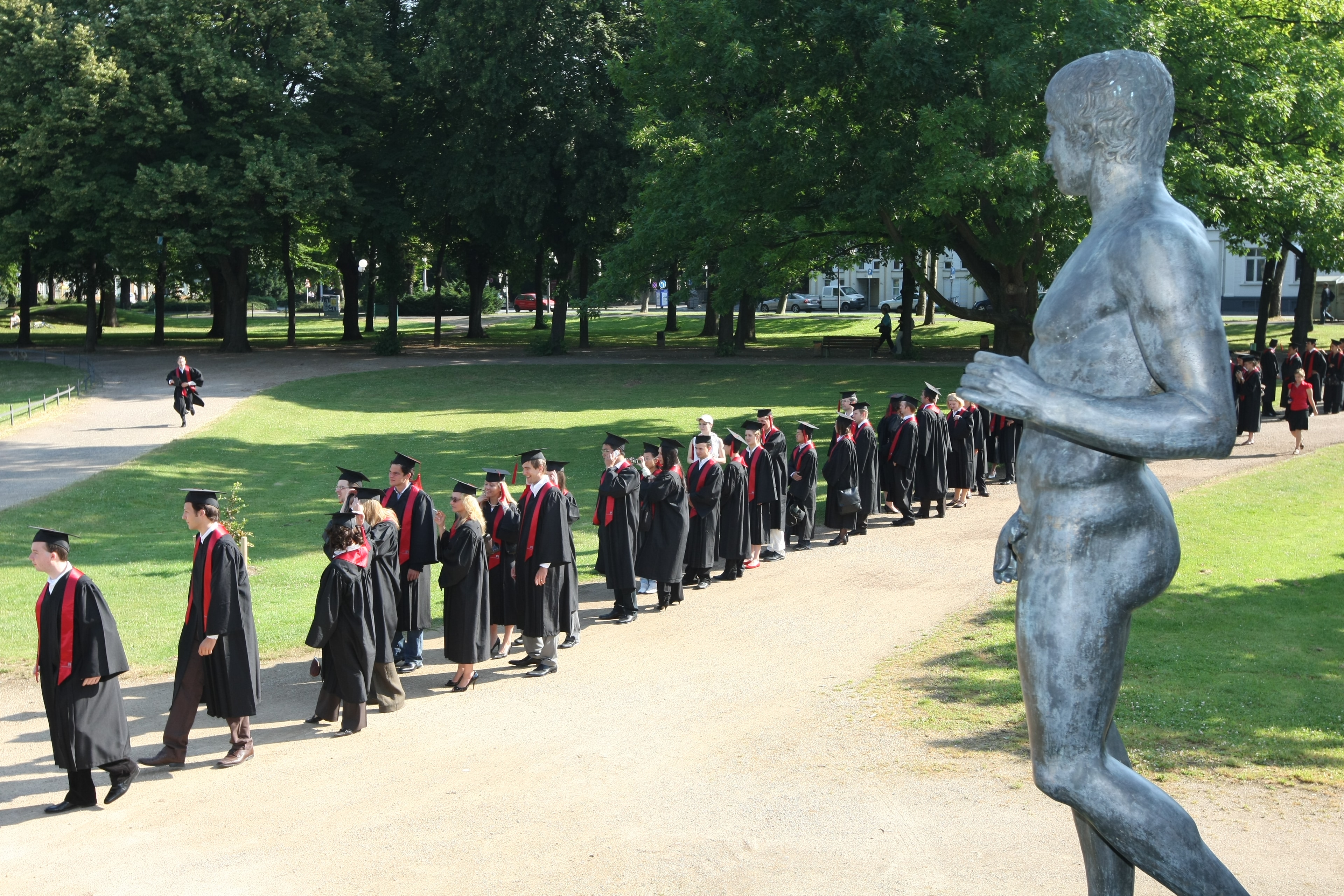 Absolventen im Hofgarten in Talaren mit roten Schärpen