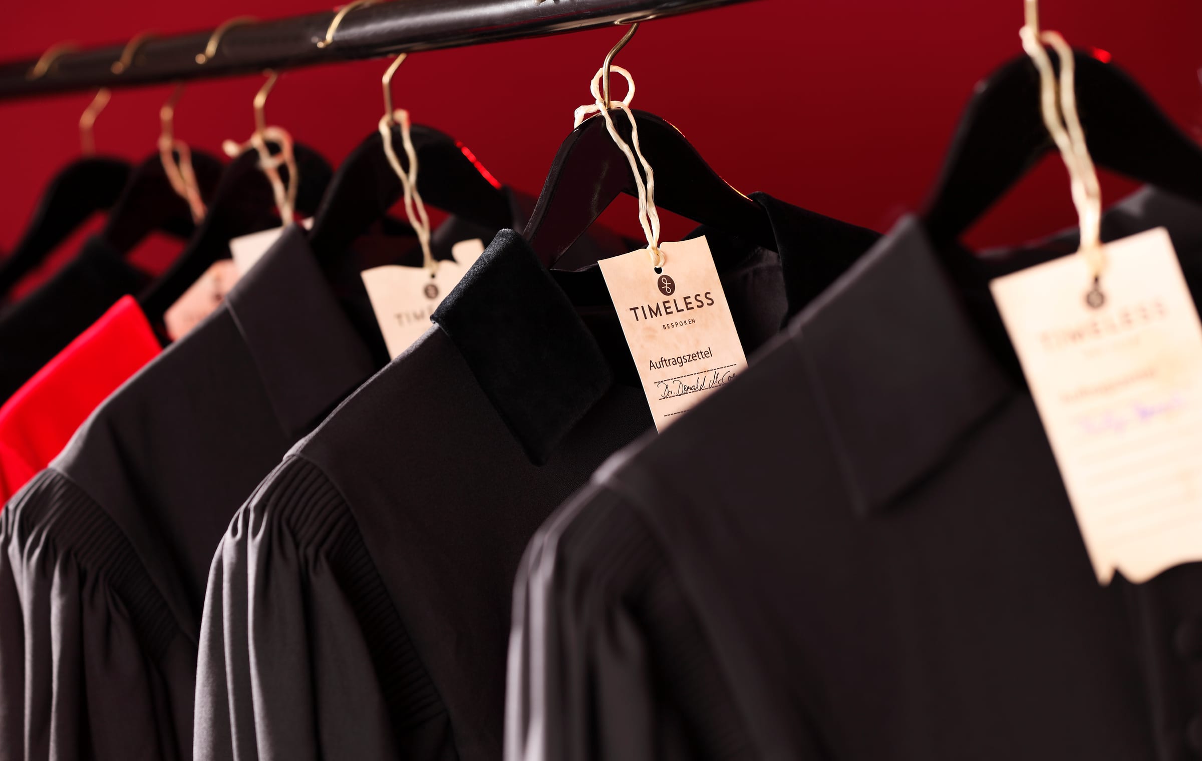 Schwarze Roben auf Kleiderbügeln im Atelier, mit Auftragszetteln versehen