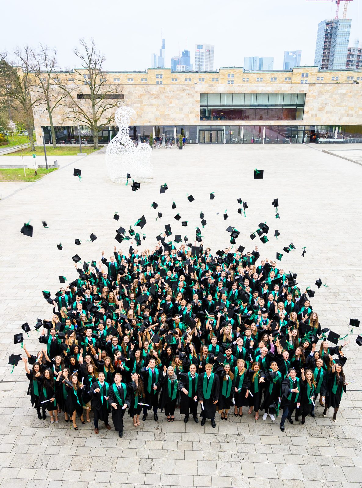 Absolventinnen und Absolventen mit grünen Schärpen vor der Frankfurter Skyline